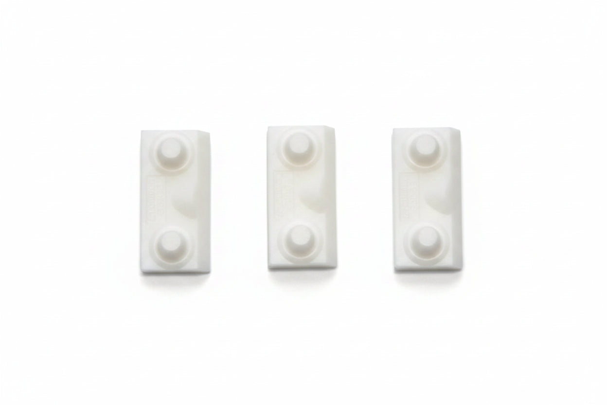 Three small white rectangular plastic pieces with circular raised details, arranged side by side on a textured blue background.