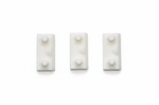 Three small white rectangular plastic pieces with circular raised details, arranged side by side on a textured blue background.